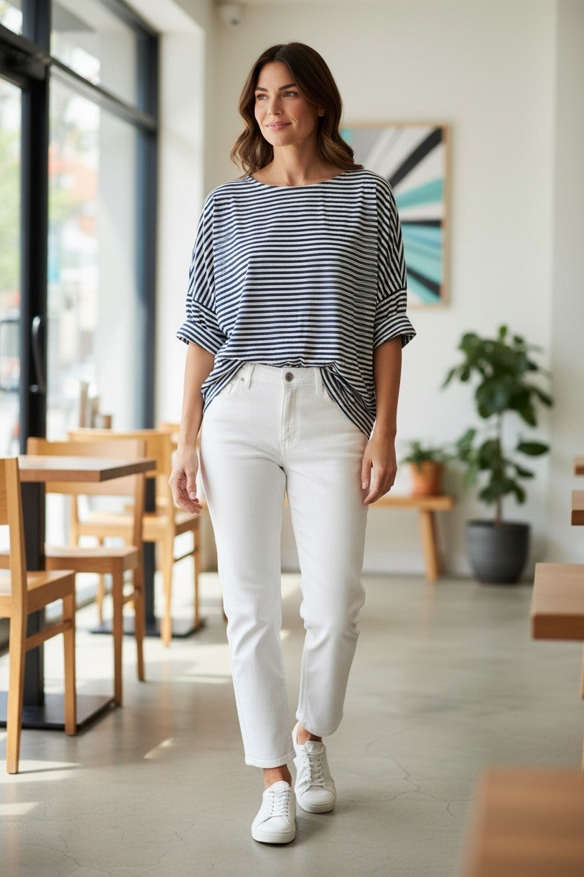 Woman in a striped shirt and white pants walking in a modern cafe.