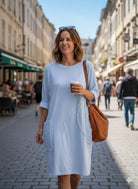 Woman in a light blue dress walking down a city street holding a coffee cup.