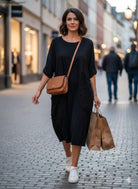 Woman in a black dress with a brown handbag walking on a street.