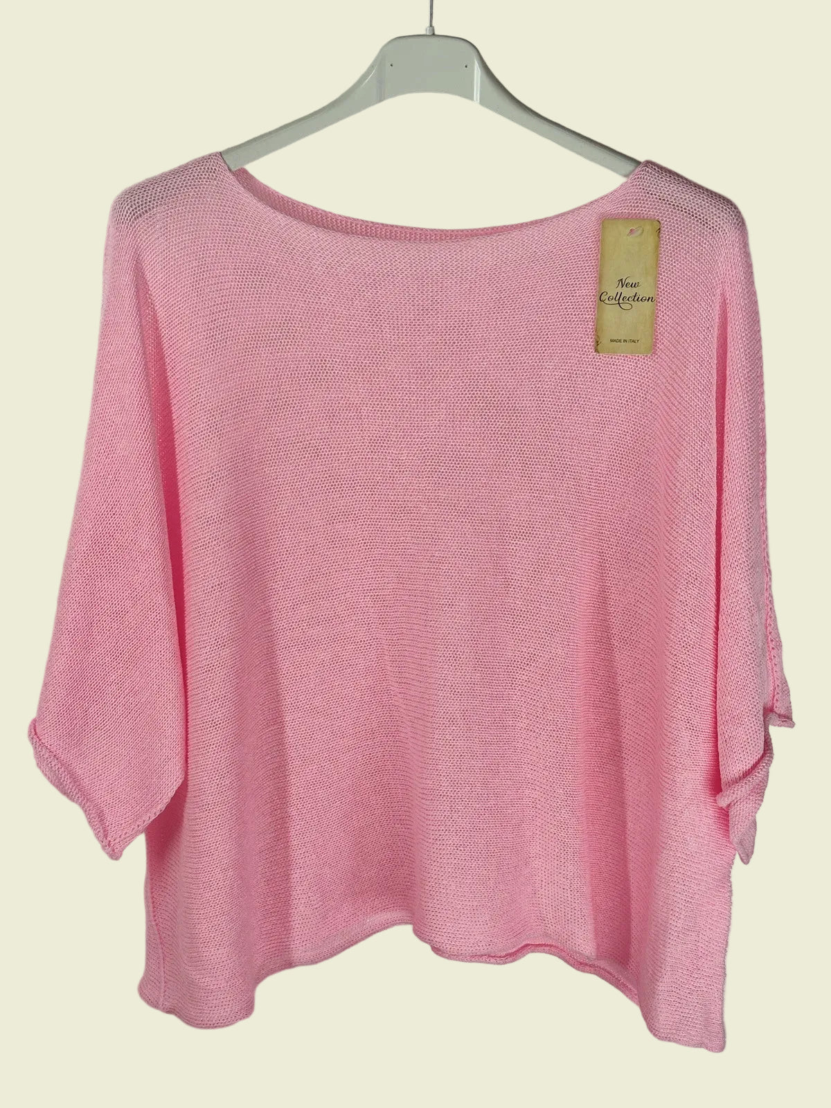 Pink sweater on a hanger with a visible tag against a neutral background