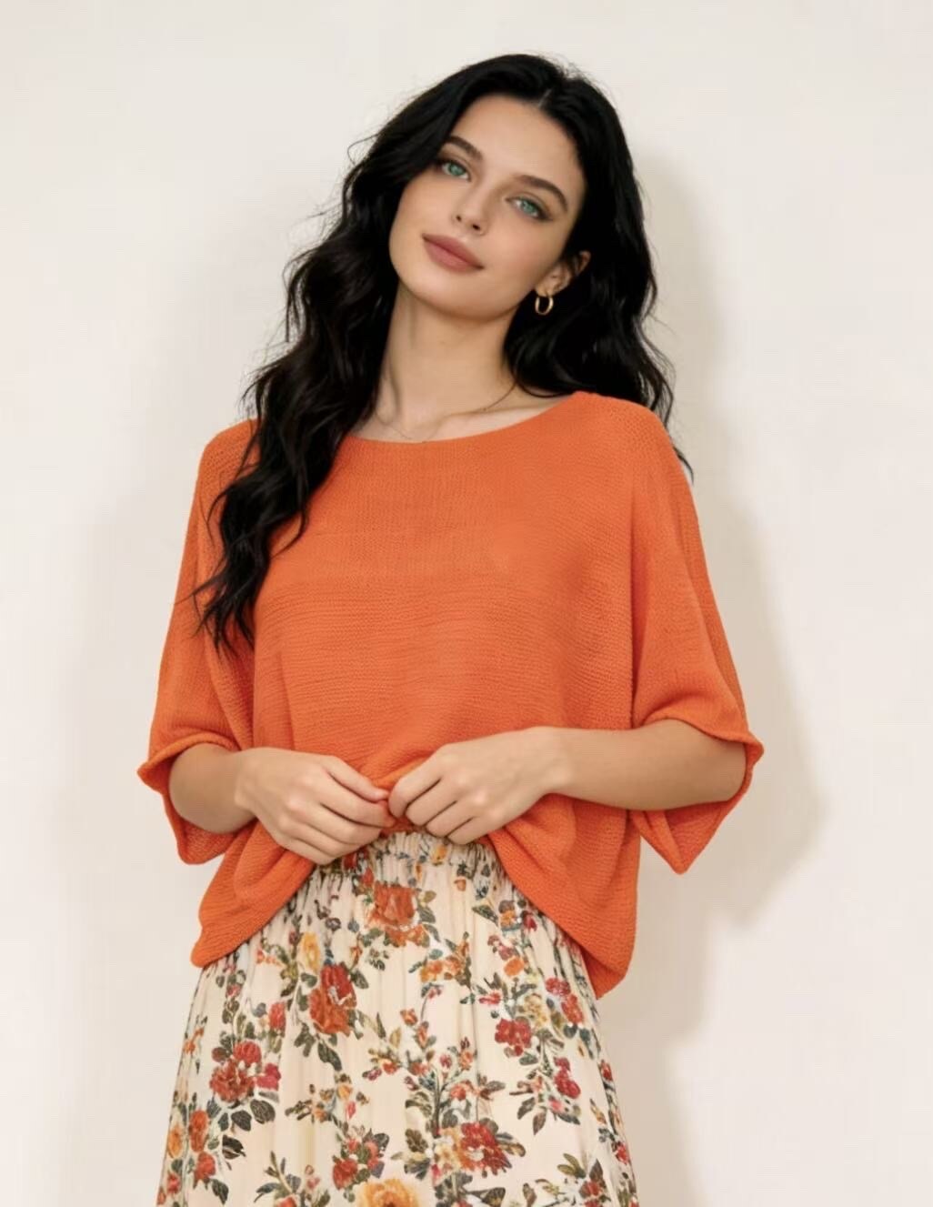 Woman wearing an orange top and floral skirt against a white background