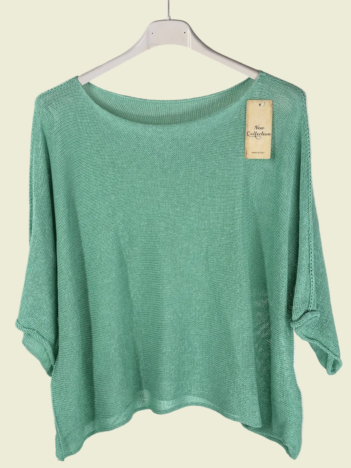 Green sweater on a hanger with a visible tag against a textured wall.